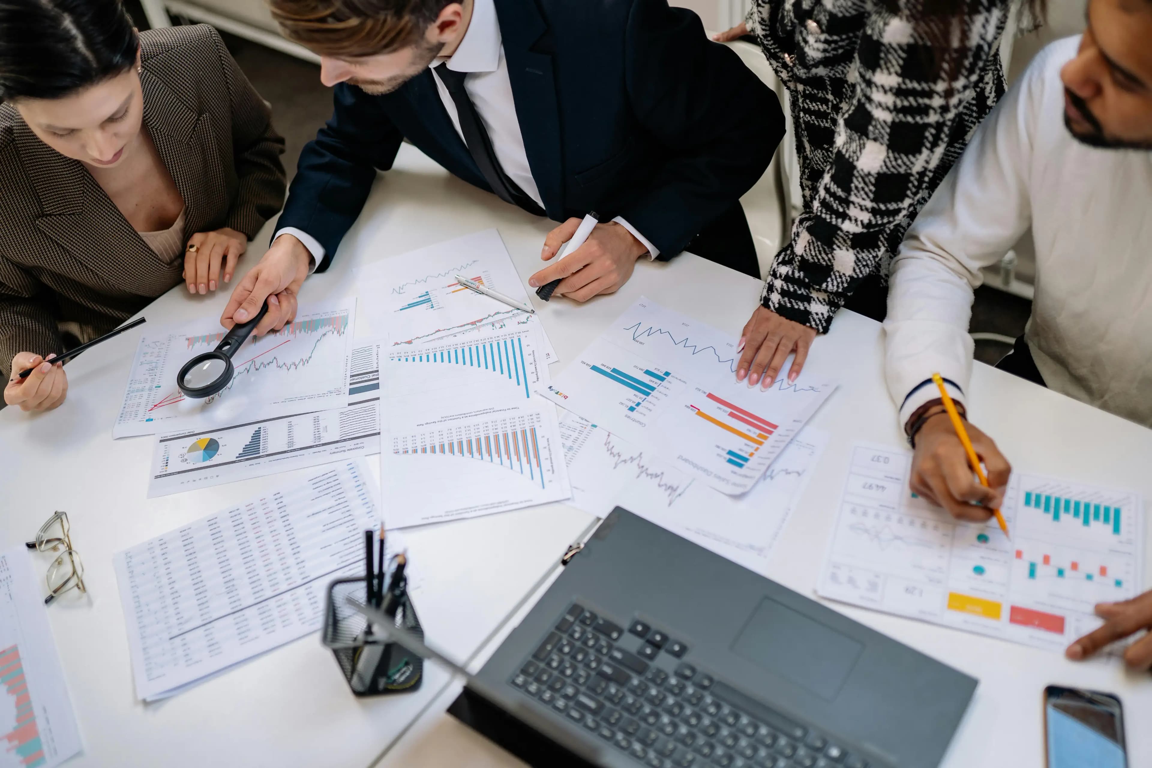 Four business professionals gathered around a desk reviewing charts and paperwork, analyzing data and compliance requirements, illustrating expert teamwork in obtaining business licenses.