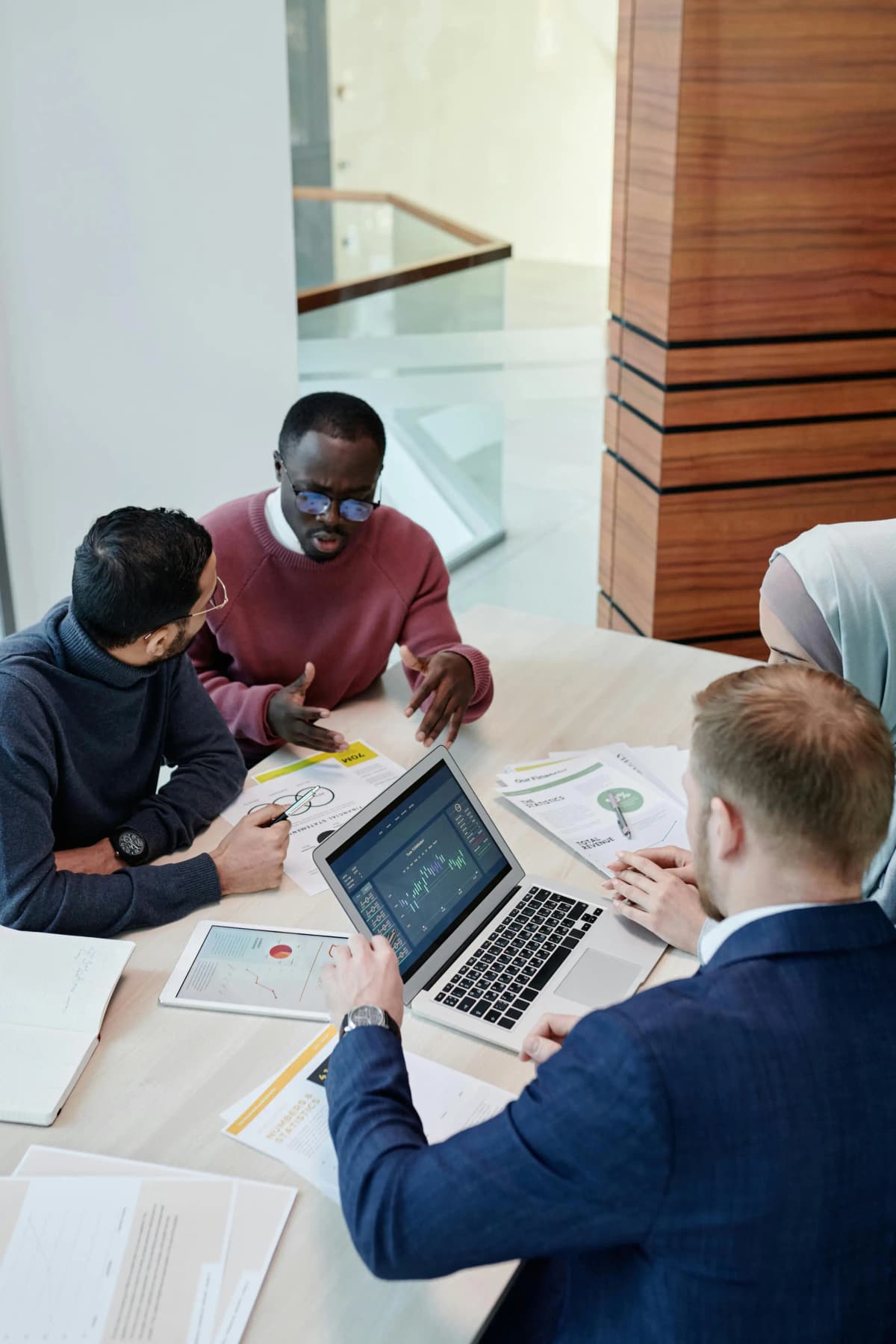 Four business professionals collaborating around a desk with a laptop and business documents, actively discussing and reviewing graphs, illustrating teamwork and strategic planning for creating an operating agreement.