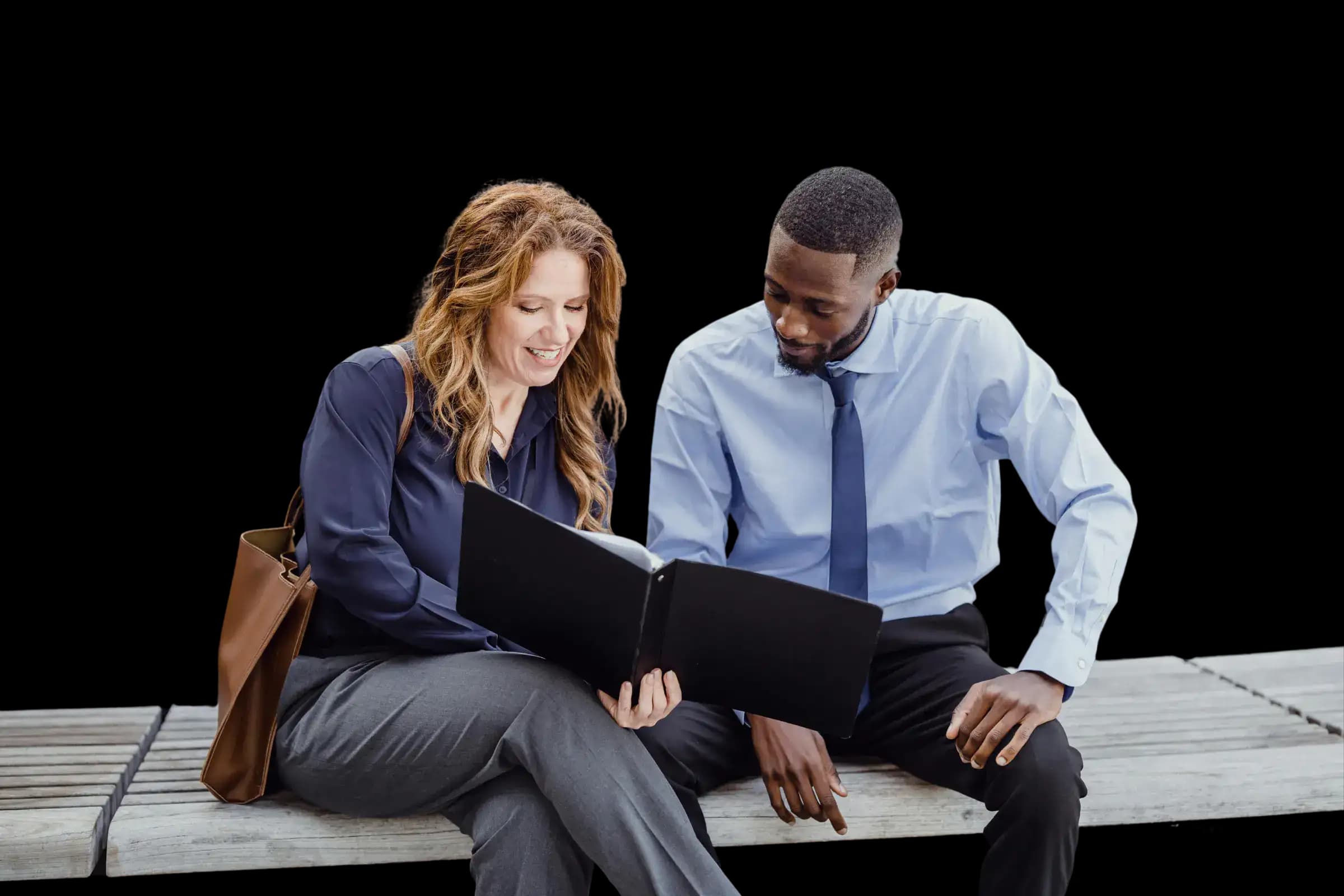 Two business professionals sitting on a bench, one holding an open folder and pointing at a document while the other looks on and smiles, illustrating collaborative review and agreement for trademark registration and brand protection.
