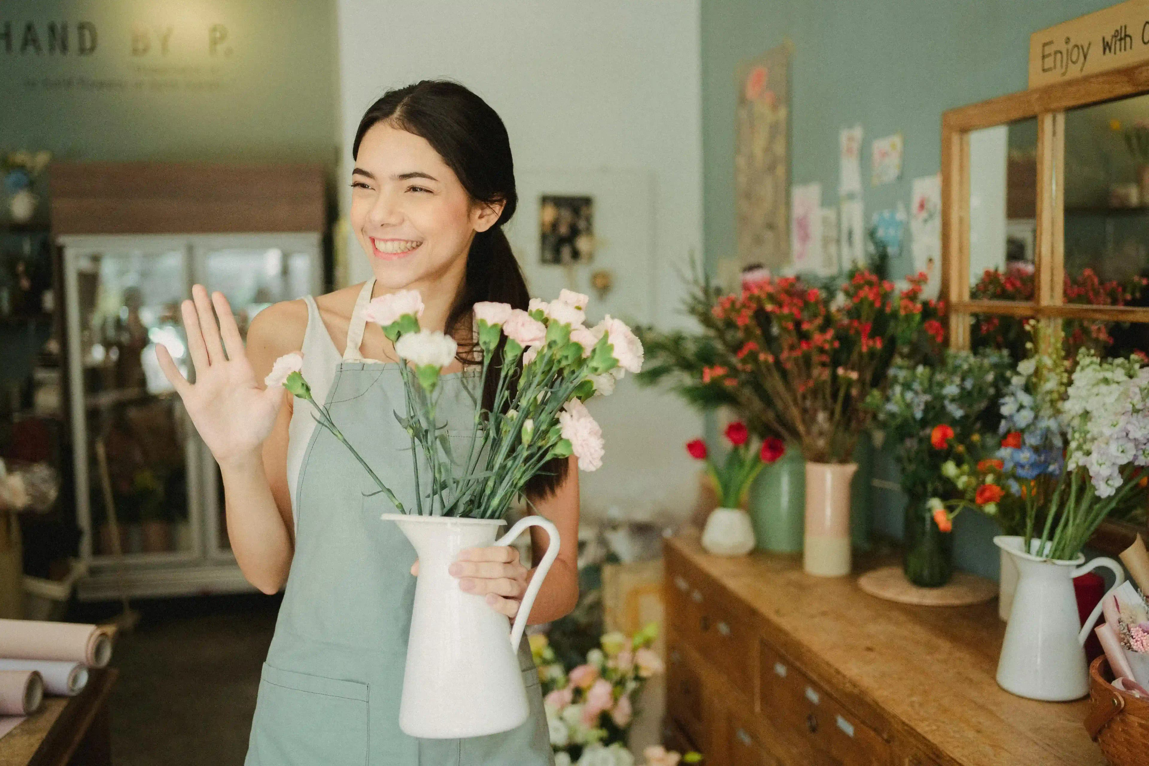 Smiling flower shop owner waving, a successful small business benefiting from expert annual report services.