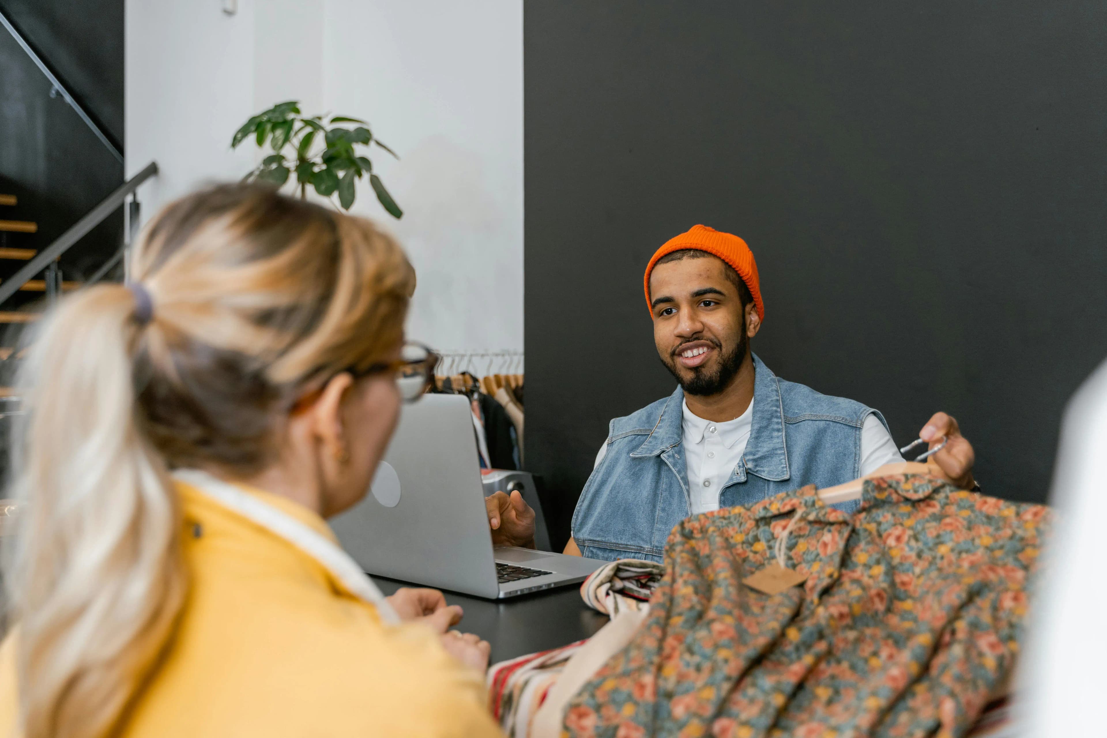 Boutique owner at a counter with a laptop assisting a customer, representing a retail small business that requires an Employer Identification Number.