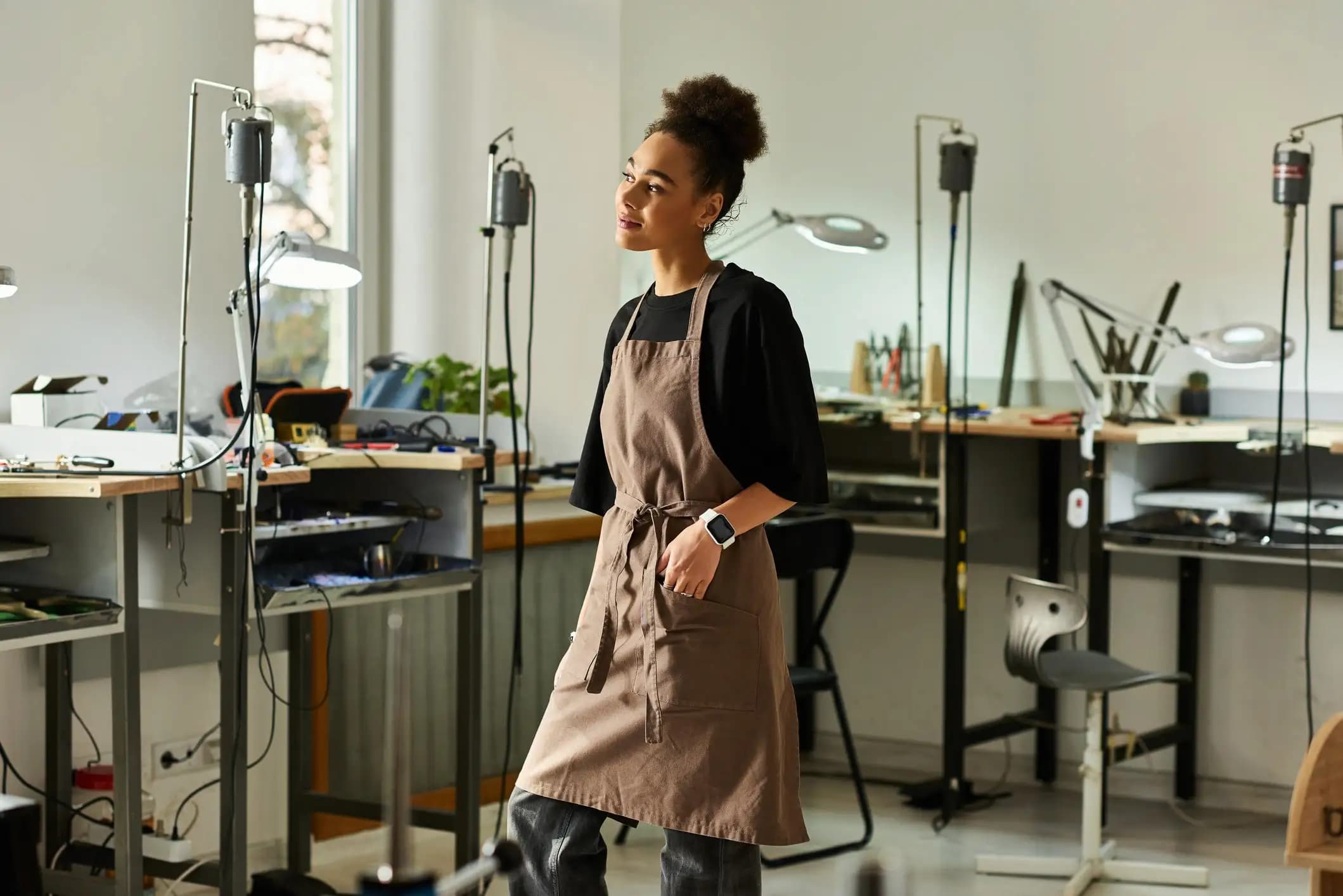 Thoughtful woman in an apron standing in her jewelry workshop, preparing to foreign qualify LLC.