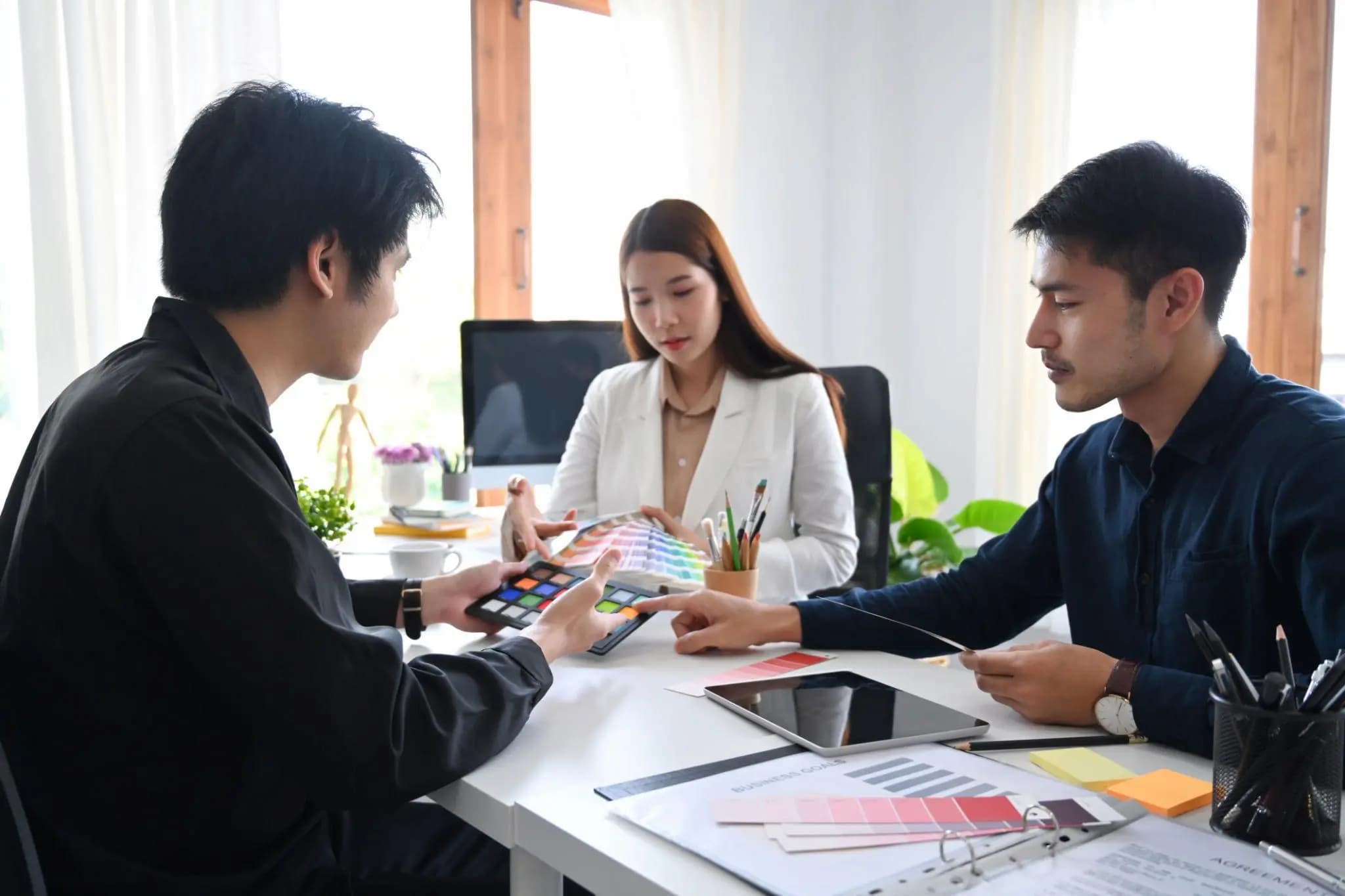 Graphic designers and a client reviewing color swatches and business goals at an office desk.