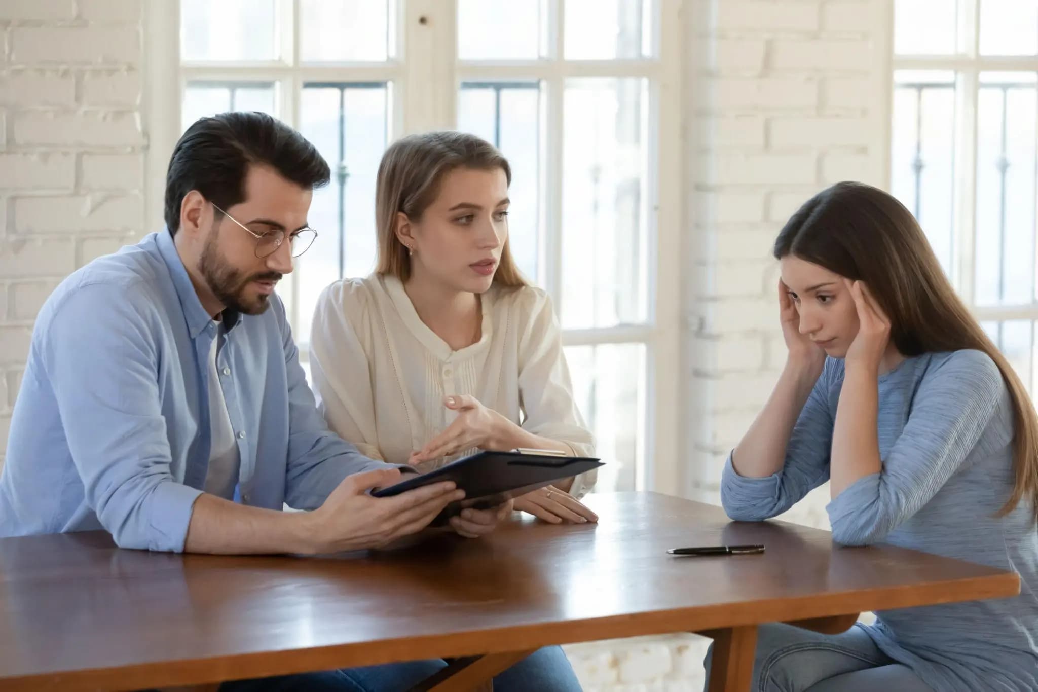 Stressed woman holding her head as colleagues review an annual report to reinstate a Florida corporation.